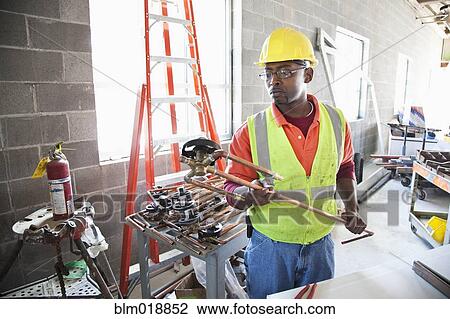 Stock Image - African American construction worker examining pipe. Fotosearch
