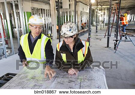 Architects reading blueprints at construction site View Large Photo Image Stock Photo - Architects reading blueprints at construction site. Fotosearch