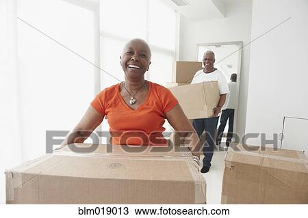 Stock Image - Black couple carrying boxes in new home. Fotosearch