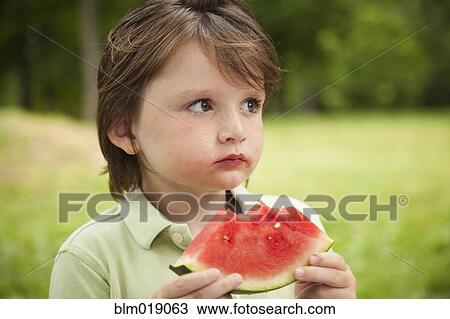 Stock Image - Caucasian boy eating watermelon outdoors. Fotosearch
