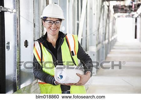 Stock Image - Caucasian construction worker carrying blueprints. Fotosearch