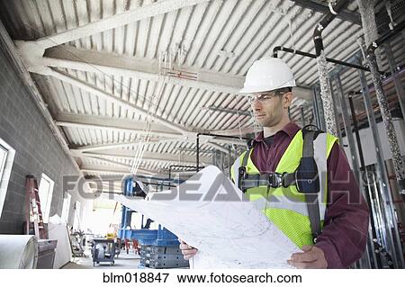 Stock Photo - Caucasian construction worker reading blueprints. Fotosearch