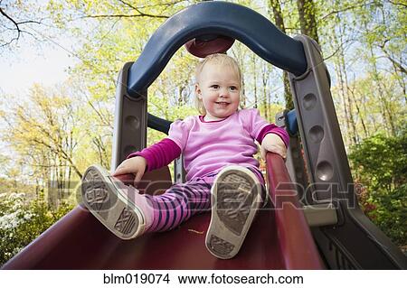 Picture - Caucasian girl playing on slide outdoors. Fotosearch