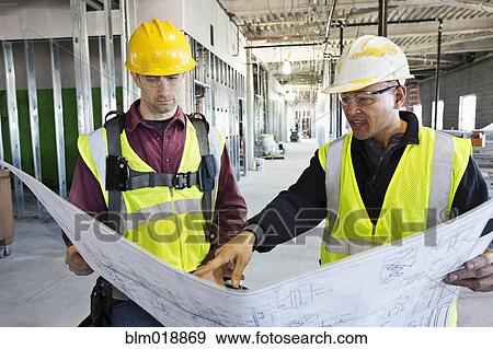 Construction workers reading blueprints at construction site View Large Photo Image Stock Photo - Construction workers reading blueprints at construction site. Fotosearch
