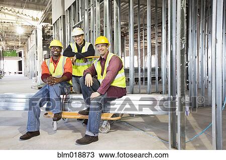 Stock Image - Construction workers smiling at construction site. Fotosearch