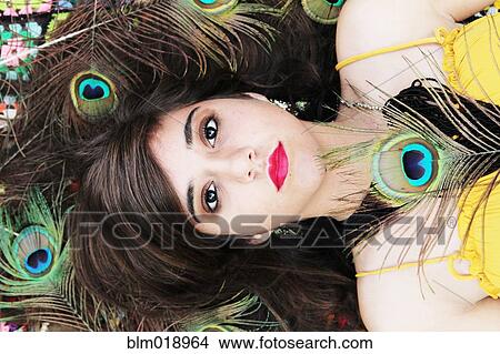 Picture - Hispanic girl surrounded by peacock feathers. Fotosearch