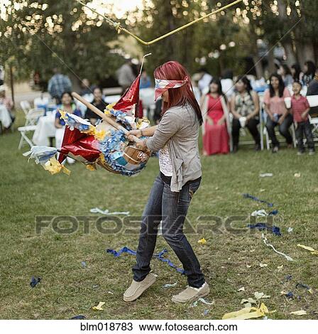 Stock Image - Hispanic woman batting at pinata. Fotosearch