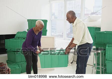 Stock Photo - Older Black couple carrying boxes in new home. Fotosearch