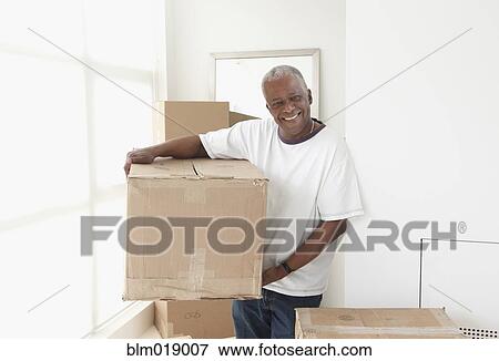 Stock Photo - Older Black man carrying box in new home. Fotosearch