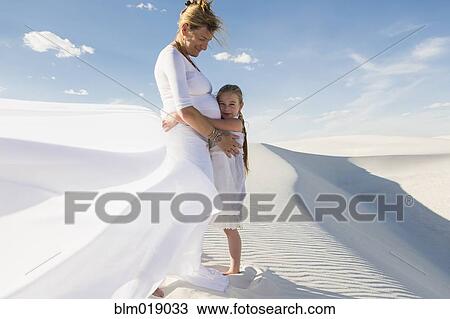 Stock Image - Pregnant Caucasian mother and daughter hugging in desert. Fotosearch