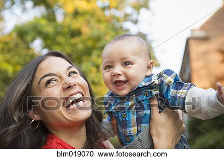 Stock Image - Smiling mother holding baby outdoors. Fotosearch