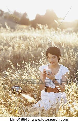 Stock Photography - Thai woman using cell phone in tall grass. Fotosearch