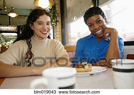 Stock Image - Women laughing in restaurant booth. Fotosearch