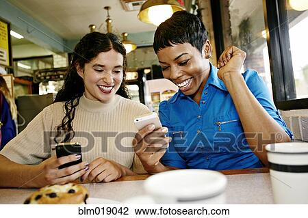 Stock Image - Women using cell phones in restaurant. Fotosearch