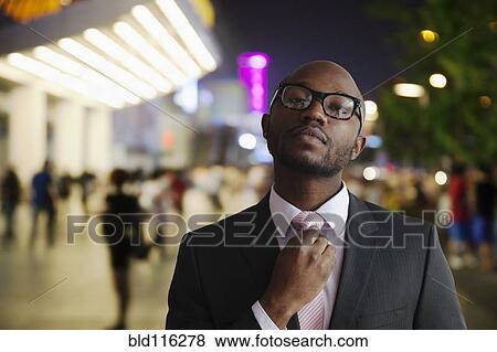 Stock Photo - Black businessman adjusting tie on city street. Fotosearch