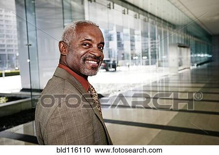 Stock Image - Black businessman smiling in office corridor. Fotosearch