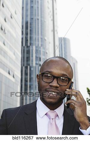 Stock Photo - Black businessman talking on cell phone on city street. Fotosearch