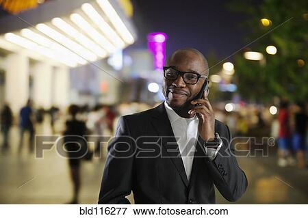 Stock Photo - Black businessman talking on cell phone on city street. Fotosearch