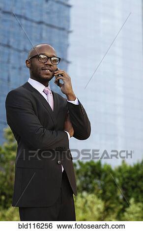 Stock Photograph - Black businessman talking on cell phone on city street. Fotosearch