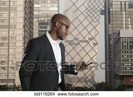 Picture - Black businessman using cell phone on city street. Fotosearch