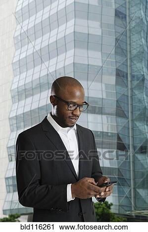 Stock Image - Black businessman using cell phone on city street. Fotosearch