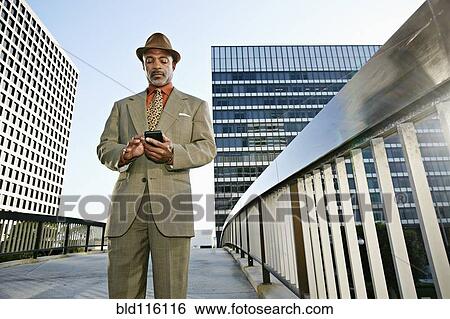 Stock Photograph - Black businessman using cell phone on urban walkway. Fotosearch