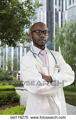 Stock Image - Black doctor standing in urban park. Fotosearch