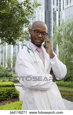 Stock Image - Black doctor talking on cell phone in urban park. Fotosearch