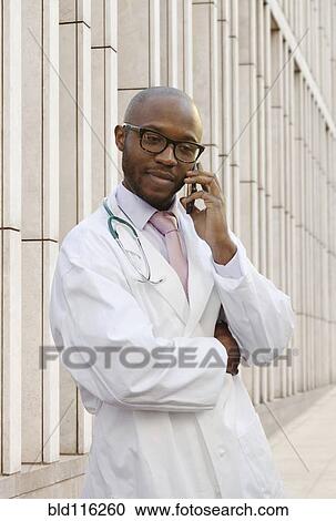 Stock Image - Black doctor talking on cell phone on city street. Fotosearch