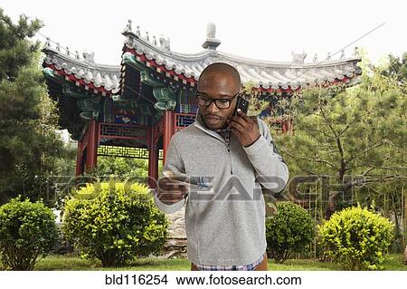 Picture - Black man reading map on city street, Beijing, Beijing, China. Fotosearch