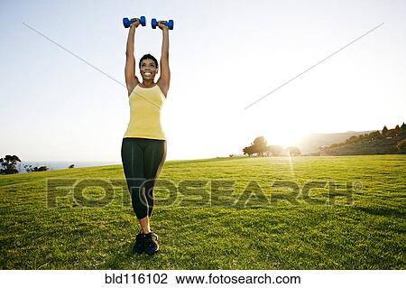 Stock Image - Black woman lifting weights in field. Fotosearch