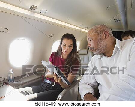 Stock Photo - Business people using digital tablet on airplane. Fotosearch