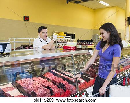 Stock Photo - Butcher serving customer at meat counter of grocery store. Fotosearch