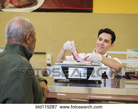 Stock Photo - Butcher serving customer meat counter of grocery store. Fotosearch