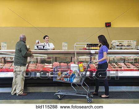 Stock Photo - Butcher serving customers at meat counter of grocery store. Fotosearch