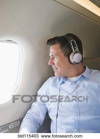 Stock Image - Caucasian businessman listening to headphones on airplane. Fotosearch