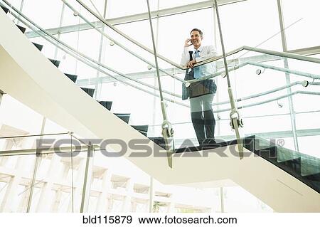 Stock Photo - Caucasian businessman on cell phone on office staircase. Fotosearch