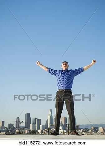 Stock Image - Caucasian businessman standing on urban rooftop. Fotosearch