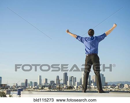 Stock Image - Caucasian businessman standing on urban rooftop. Fotosearch