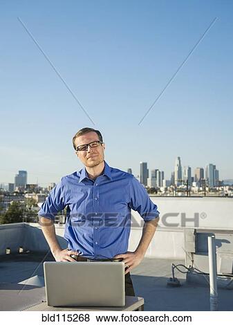 Stock Photo - Caucasian businessman using laptop on urban rooftop. Fotosearch