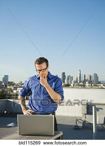 Stock Photo - Caucasian businessman using laptop on urban rooftop. Fotosearch
