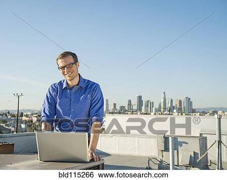 Stock Photograph - Caucasian businessman using laptop on urban rooftop. Fotosearch