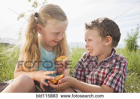 Stock Image - Caucasian children sharing fruit outdoors. Fotosearch