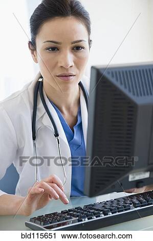 Stock Image - Caucasian doctor using computer at desk. Fotosearch