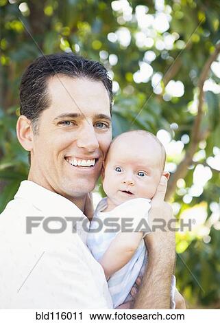 Stock Image - Caucasian father holding baby outdoors. Fotosearch