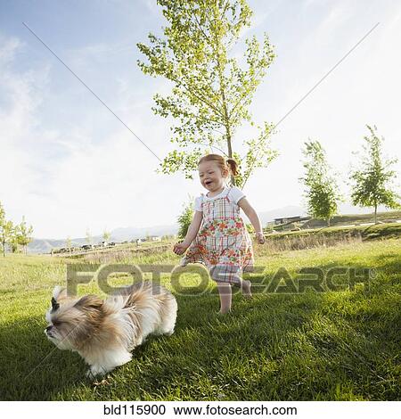 Stock Image - Caucasian girl chasing dog in grass. Fotosearch