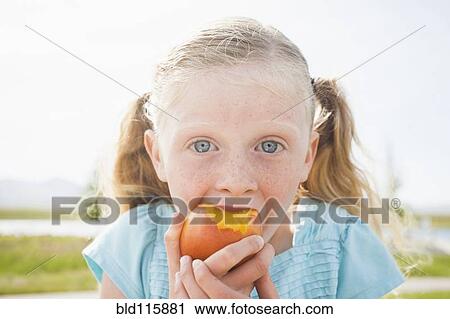 Stock Image - Caucasian girl eating fruit outdoors. Fotosearch