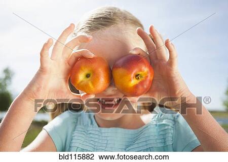 Stock Image - Caucasian girl holding fruit over eyes. Fotosearch