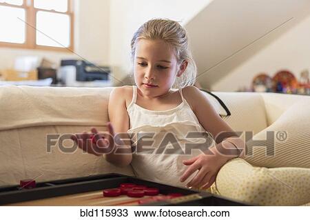 Stock Image - Caucasian girl playing backgammon on sofa. Fotosearch