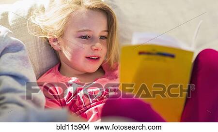 Picture - Caucasian girl reading on sofa. Fotosearch